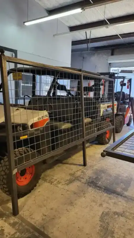 Inside the Aztec Fence and Ornamental Iron shop: a custom welded-wire cage frame built around a Bobcat UTV, a forklift behind it and the Aztec sticker on the frame