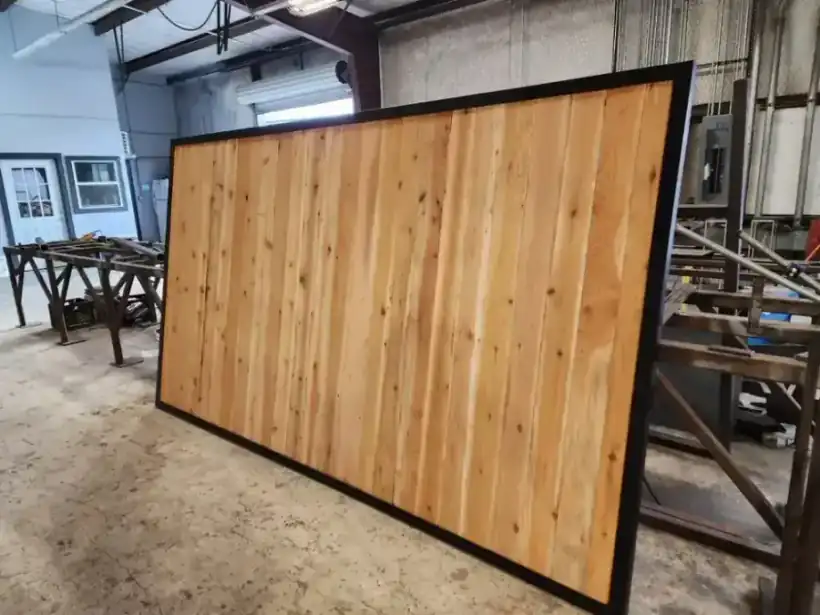 A finished cedar and steel gate leaf standing in the Aztec fabrication shop, welding tables behind it