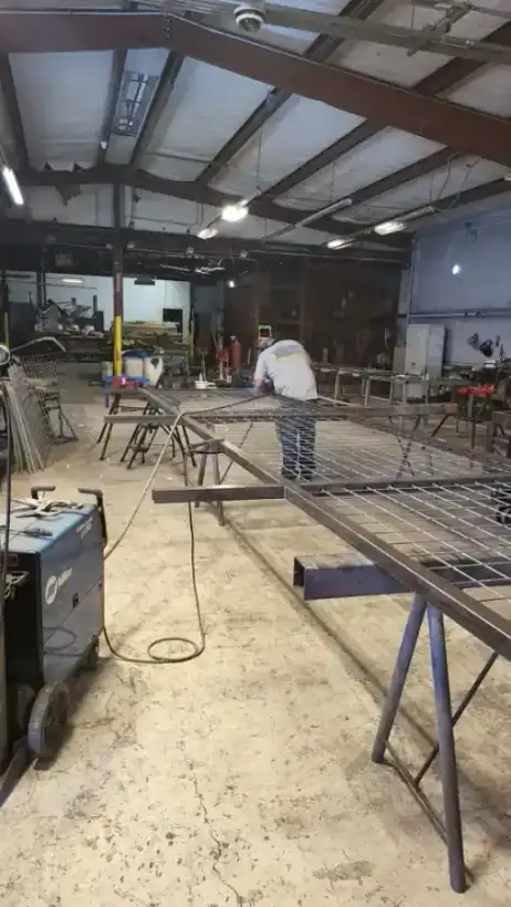 A welder working a large gate frame on sawhorses inside the Aztec Fence and Ornamental Iron welding shop