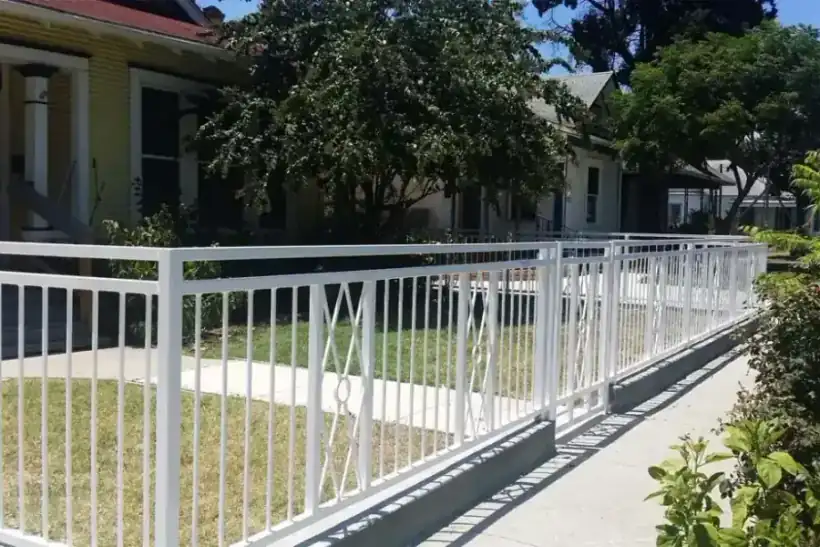 A white ornamental iron fence with diamond panels running along a street of historic San Antonio cottages