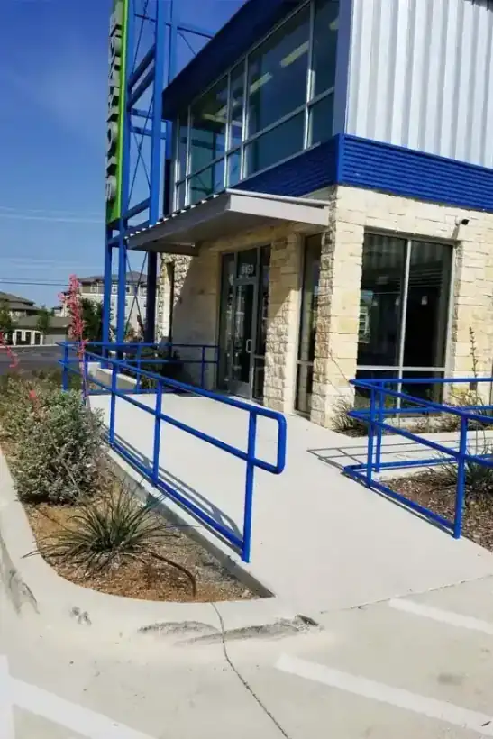 A blue steel pipe handrail and ADA ramp at a stone-and-metal commercial building