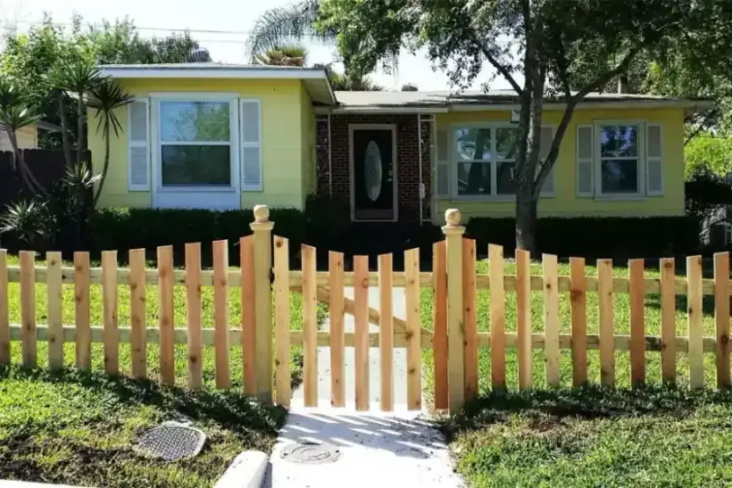 A new cedar picket fence and matching gate in front of a yellow bungalow
