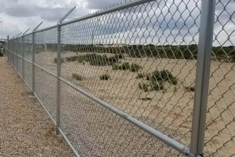 Galvanized chain-link fencing with barbed-wire arms at a coastal industrial site